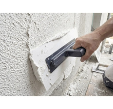 Un artisan applique de l'enduit sur un mur à l'aide d'une taloche.