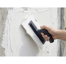 Une personne applique de l'enduit sur un mur avec une taloche.