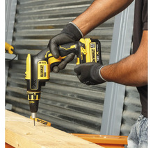 Ein Handwerker verwendet einen gelben Akku-Trockenbauschrauber von DeWalt, um eine Schraube in ein Holzbrett zu schrauben.