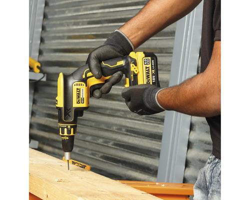 Ein Handwerker verwendet einen gelben Akku-Trockenbauschrauber von DeWalt, um eine Schraube in ein Holzbrett zu schrauben.