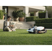 Un homme lit un livre dans le jardin à côté d'un robot tondeuse.