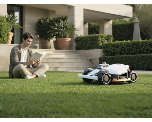 Un homme lit un livre dans le jardin à côté d'un robot tondeuse.
