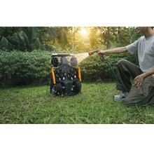 Un homme nettoie un robot tondeuse avec un tuyau d'arrosage dans le jardin.