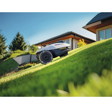 Robot tondeuse sur une pelouse devant une maison.