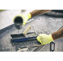 Une personne verse de la peinture dans un bac à peinture à côté d'un rouleau à peinture et d'un mastic