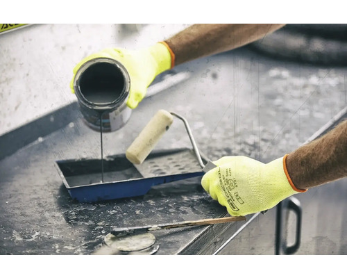 Une personne verse de la peinture dans un bac à peinture à côté d'un rouleau à peinture et d'un mastic