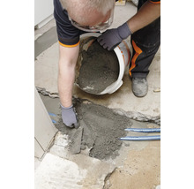 Handwerker füllt Reparaturmörtel mit einer Kelle in ein Loch im Boden.