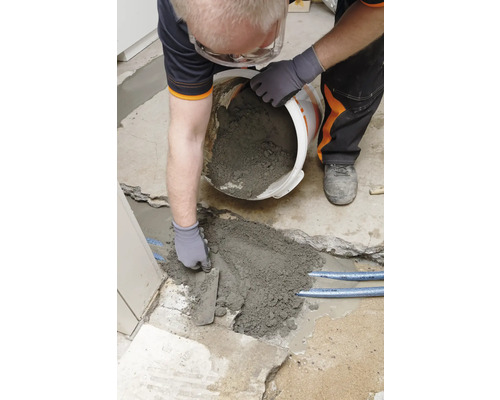 Handwerker füllt Reparaturmörtel mit einer Kelle in ein Loch im Boden.