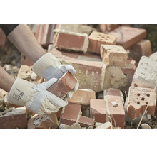 Une personne portant des gants de travail tient une brique devant une pile de briques.