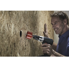 Un homme perce un trou dans une plaque de bois avec une scie trépan.