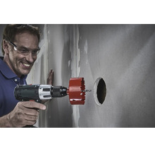 Un homme perce un trou dans un mur avec une scie cloche et une perceuse sans fil