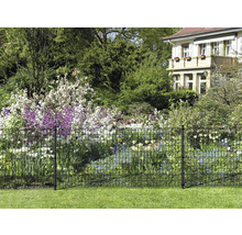 Vue du jardin avec une clôture métallique pour délimiter la propriété et des parterres de fleurs en arrière-plan.