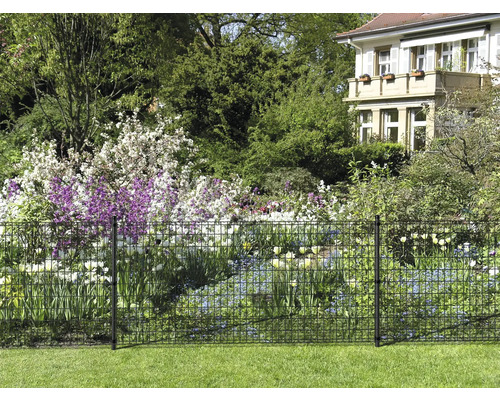 Vue du jardin avec une clôture métallique pour délimiter la propriété et des parterres de fleurs en arrière-plan.