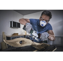 Anwender mit Atemschutzmaske, Schutzbrille und Handschuhen bearbeitet Holz mit einem Winkelschleifer