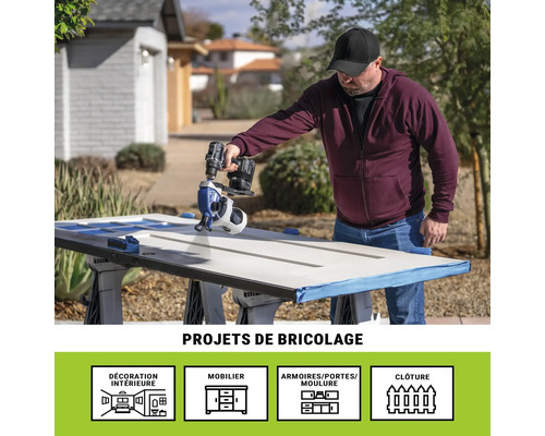 Un homme peint une porte avec un pulvérisateur de peinture à l'extérieur. Projets de bricolage.