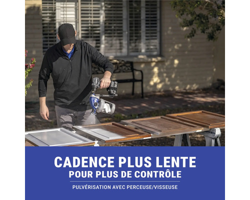 Une personne pulvérise de la peinture avec un pulvérisateur de peinture sur des portes d'armoires en bois.