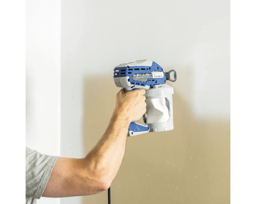 Eine Person hält eine Farbspritzpistole vor eine Wand