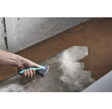 Main avec un grattoir triangulaire nettoyant une surface métallique