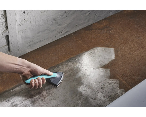 Main avec un grattoir triangulaire nettoyant une surface métallique