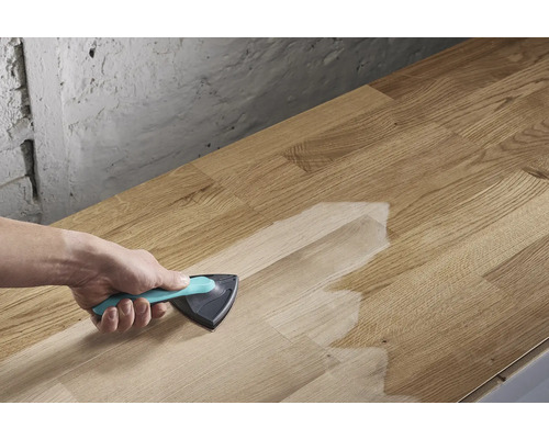 Une personne applique un traitement de surface à l'aide d'un pinceau triangulaire sur une planche de bois.