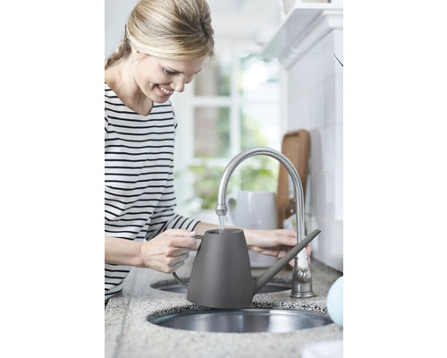 Femme remplissant un arrosoir gris à un robinet