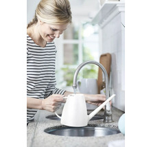 Femme remplissant un arrosoir blanc au robinet de la cuisine.