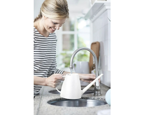Femme remplissant un arrosoir blanc au robinet de la cuisine.