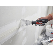 Une personne enduit un mur de mastic et d'une spatule de Rautner.