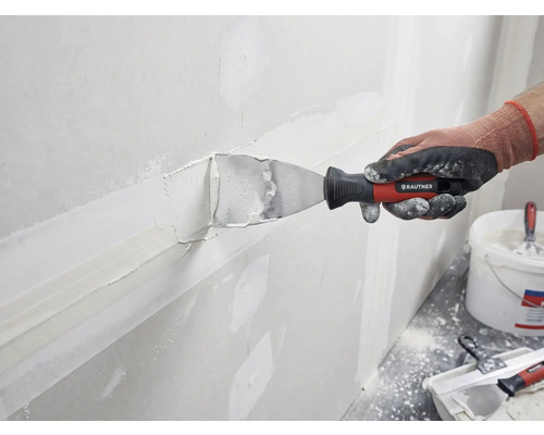 Une personne enduit un mur de mastic et d'une spatule de Rautner.