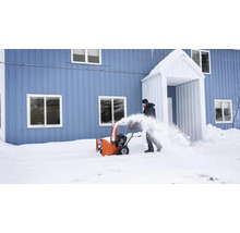 Eine Person benutzt eine Schneefräse vor einem Haus, um Schnee zu räumen.