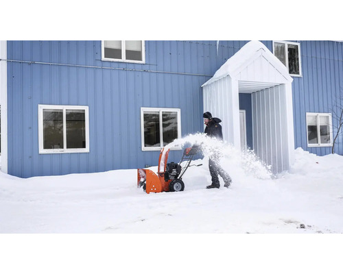 Eine Person benutzt eine Schneefräse vor einem Haus, um Schnee zu räumen.