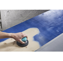 Une personne ponce une surface en bois bleue avec une ponceuse excentrique.