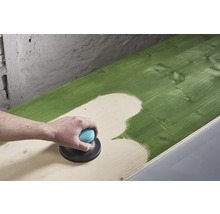 Une personne ponce une surface en bois peinte en vert avec une ponceuse excentrique.