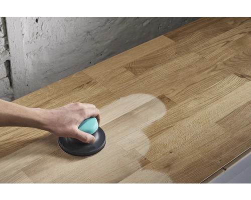 Une personne ponce une plaque de bois avec une ponceuse excentrique.