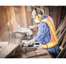 Eine Person mit persönlicher Schutzausrüstung, die eine Kappsäge zum Schneiden von Holz verwendet.