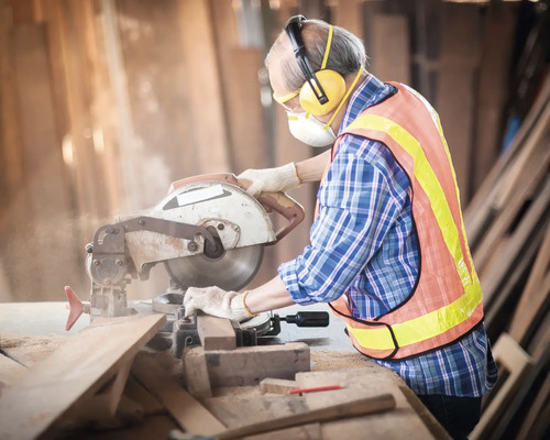 Eine Person mit persönlicher Schutzausrüstung, die eine Kappsäge zum Schneiden von Holz verwendet.