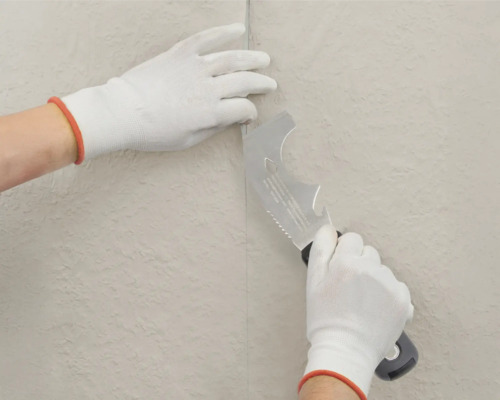 Hände mit Handschuhen bearbeiten eine Tapete mit einem Multifunktionswerkzeug