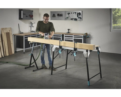 Mann fräst Holz auf einer Werkbank mit Schraubzwingen in einer Werkstatt