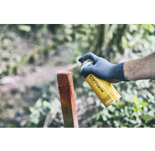 Une personne vaporise un poteau en bois avec un aérosol universel jaune