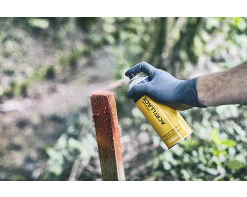 Une personne vaporise un poteau en bois avec un aérosol universel jaune