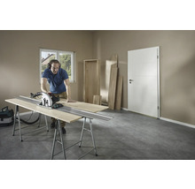 Un homme coupe du bois avec une scie circulaire sur un établi dans une pièce.