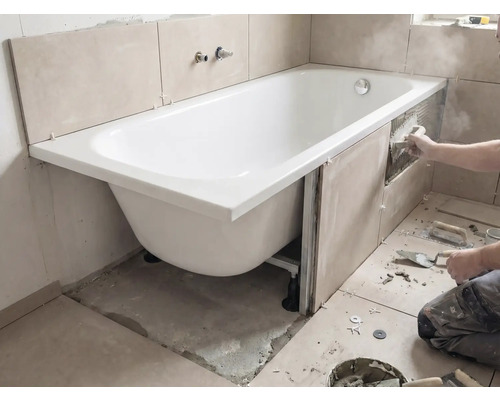 Installation d'une baignoire avec carrelage sur les murs et outils dans la salle de bains.