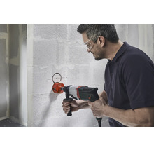 Ein Mann bohrt mit einer Lochsäge ein Loch in eine Wand.