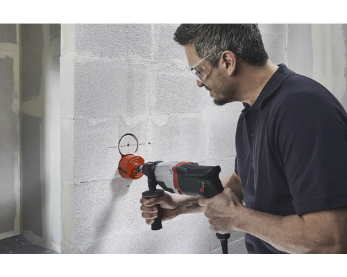 Ein Mann bohrt mit einer Lochsäge ein Loch in eine Wand.