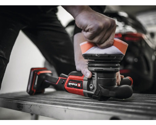 Ein Mann poliert ein Auto mit einer Poliermaschine. Die Poliermaschine ist rot und schwarz und hat ein Polierpad.