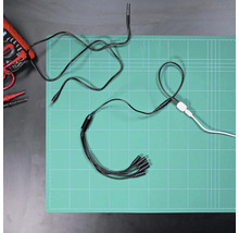 Verteilerkabel mit fünf Anschlüssen auf einer Schneidematte neben einem Multimeter und weiteren Kabeln in einer organisierten Arbeitsumgebung.