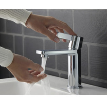 Person bedient einen glänzenden Waschtischmischer im Badezimmer