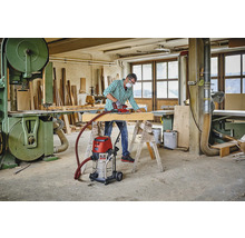 Atelier avec artisan, ponceuse, poutre en bois, établi, aspirateur industriel et scie à ruban