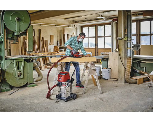 Atelier avec artisan, ponceuse, poutre en bois, établi, aspirateur industriel et scie à ruban