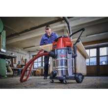Scène d'atelier avec un aspirateur eau et poussière Einhell et un homme travaillant une planche de bois